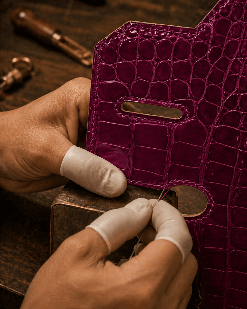 Hand-stitching gold hardware onto purple crocodile leather bag