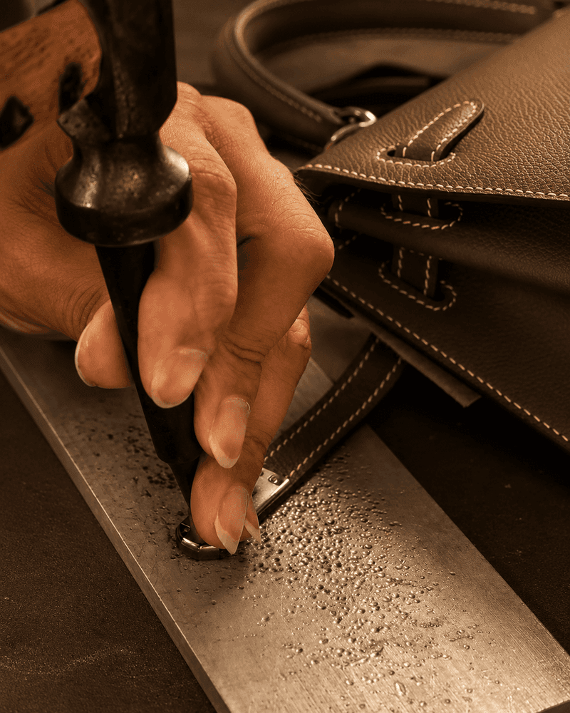 Craftsman hammering fine details on brown leather bag